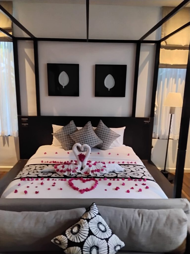 Luxurious honeymoon suite with rose petals on the bed, overlooking a tranquil pool.