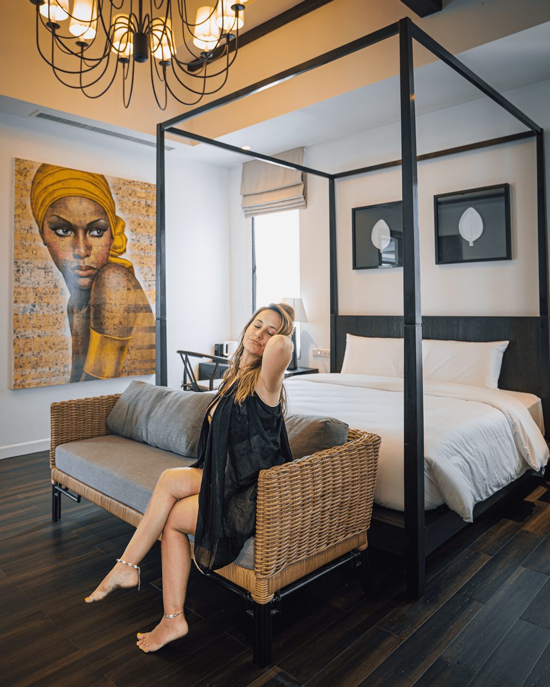 Guest relaxing in a Junior Suite with four-poster bed, chandelier and original artwork at Yao Bada Badoo, Koh Yao Yai